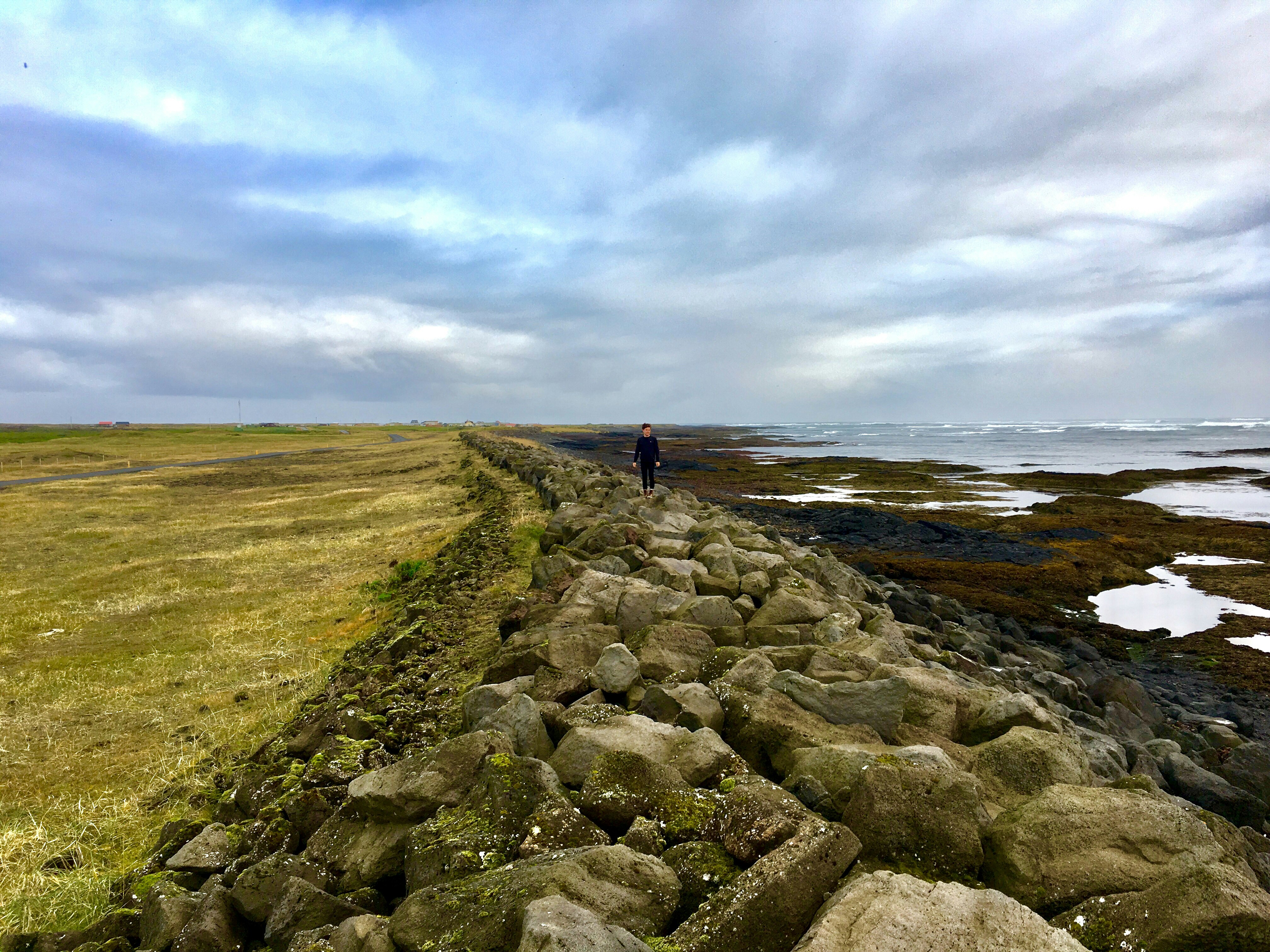 person walking on rocks near body of water under cloudy sky